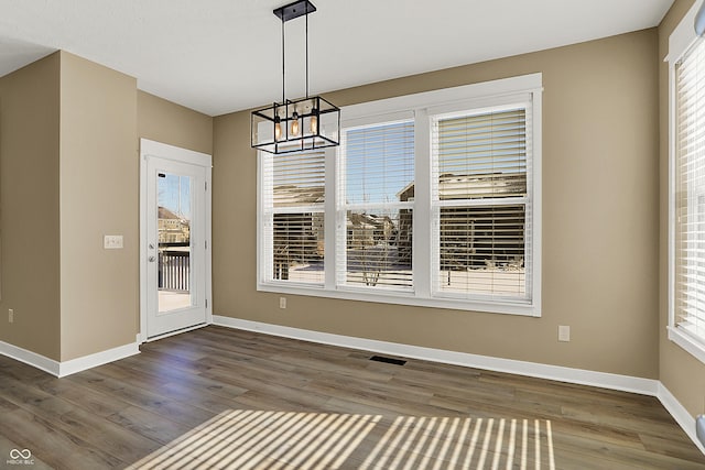 unfurnished dining area featuring a notable chandelier, wood finished floors, visible vents, and baseboards