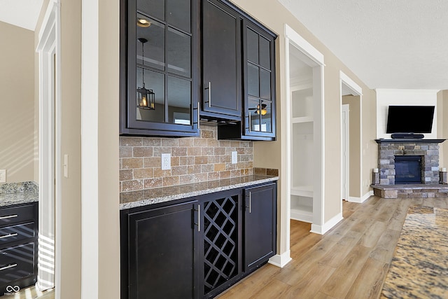 bar featuring backsplash, baseboards, a stone fireplace, and light wood finished floors