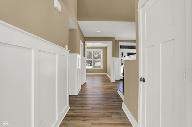 hall featuring a wainscoted wall, baseboards, and wood finished floors