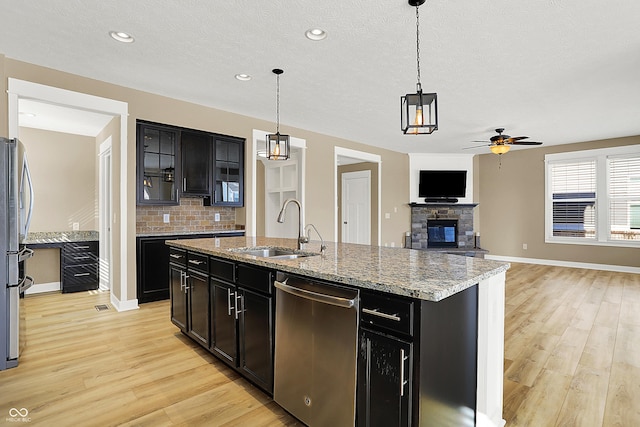 kitchen with stainless steel appliances, a fireplace, a sink, light wood-type flooring, and backsplash