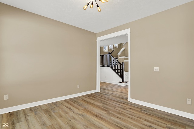 empty room featuring light wood-style floors, stairs, baseboards, and an inviting chandelier