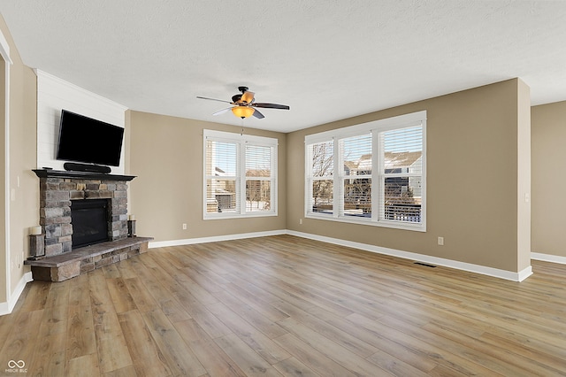 unfurnished living room featuring a textured ceiling, light wood-style flooring, a fireplace, visible vents, and a ceiling fan