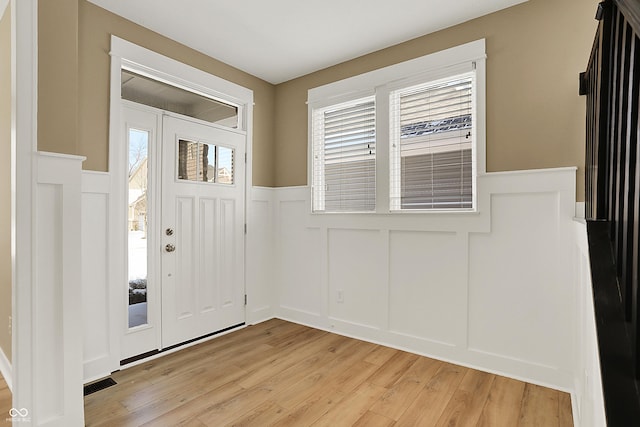 entrance foyer featuring light wood finished floors, wainscoting, visible vents, and a decorative wall