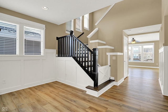 staircase featuring recessed lighting, a decorative wall, wainscoting, ceiling fan, and wood finished floors