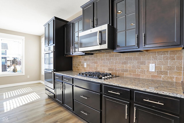 kitchen featuring light stone counters, stainless steel appliances, backsplash, light wood-style floors, and baseboards