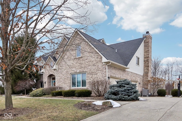 view of front of property featuring brick siding, a chimney, central AC unit, a front yard, and a garage