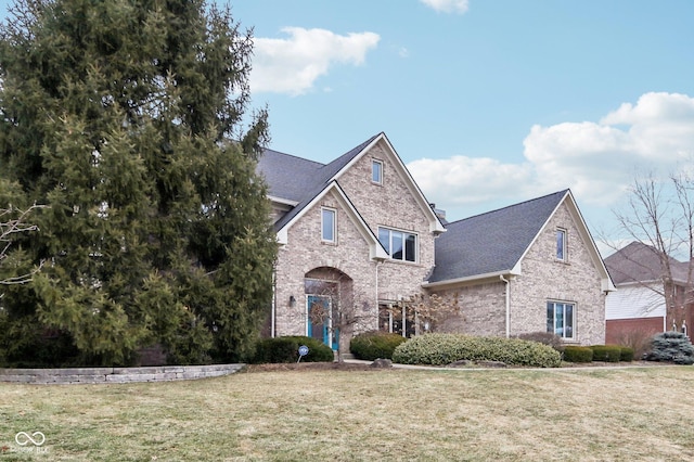 traditional home featuring brick siding, roof with shingles, and a front yard