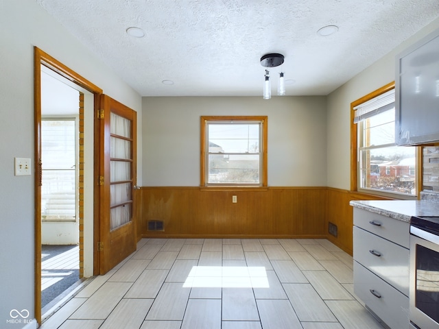 unfurnished dining area with a textured ceiling, a wealth of natural light, and wainscoting