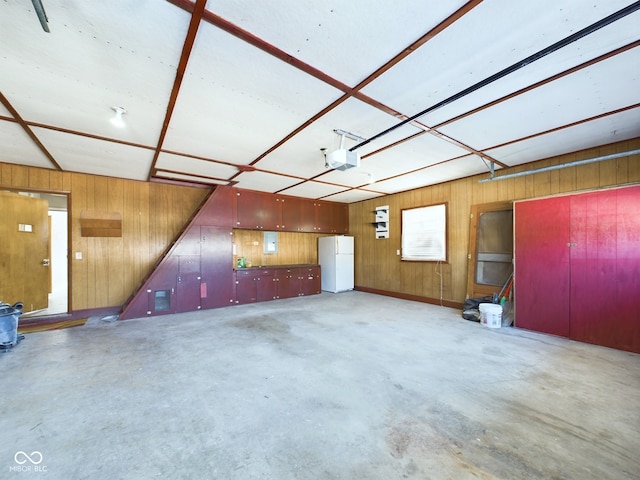 garage featuring a garage door opener, freestanding refrigerator, and wood walls