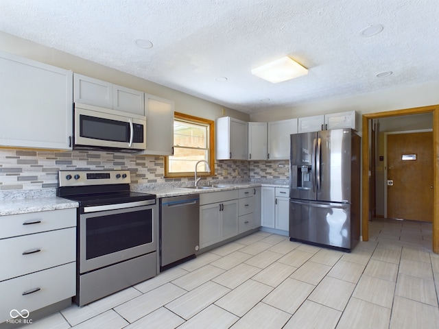 kitchen featuring tasteful backsplash, appliances with stainless steel finishes, light stone counters, gray cabinetry, and a sink