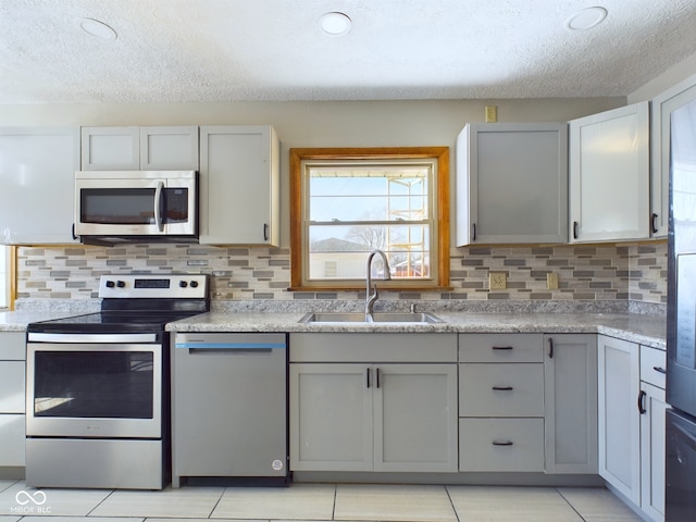 kitchen featuring light tile patterned floors, appliances with stainless steel finishes, a sink, and gray cabinetry