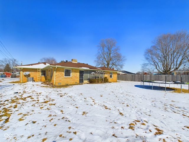 snow covered rear of property featuring a trampoline, crawl space, brick siding, and fence