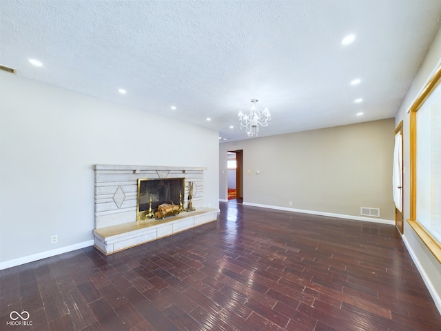 unfurnished living room featuring a textured ceiling, dark wood-style flooring, a fireplace, visible vents, and baseboards