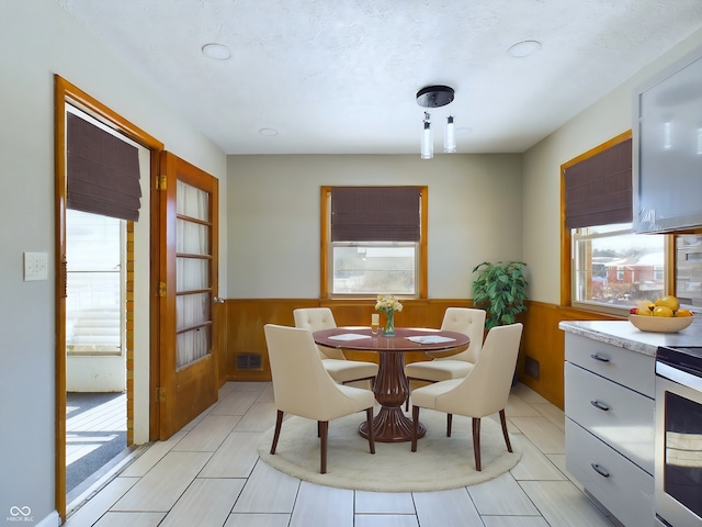 dining room featuring wood walls, visible vents, a textured ceiling, and wainscoting