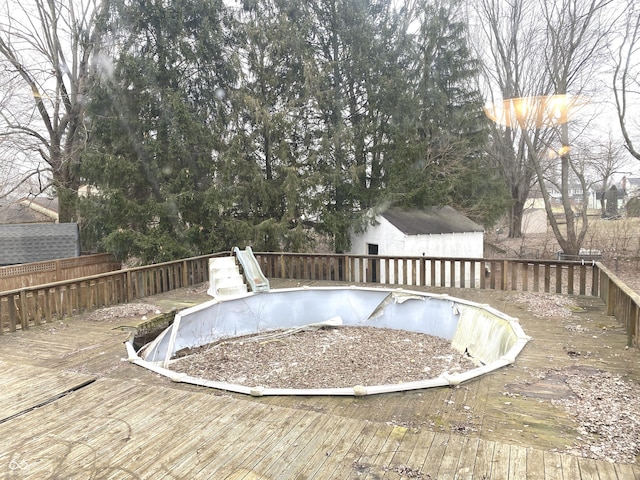 view of pool featuring a wooden deck, a fenced in pool, fence, an outdoor structure, and a shed