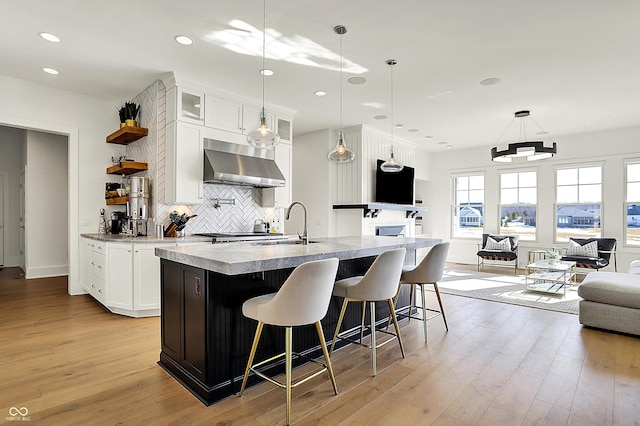 kitchen featuring wall chimney range hood, a sink, and light wood-style flooring