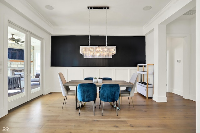 dining area with a decorative wall, wood finished floors, visible vents, ornamental molding, and an inviting chandelier