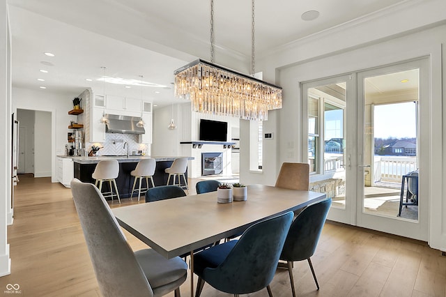 dining space with french doors, crown molding, recessed lighting, a glass covered fireplace, and light wood-type flooring