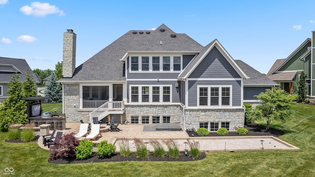 back of house featuring a yard, stone siding, a patio, and a chimney