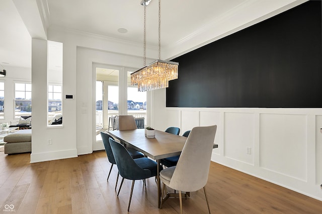 dining area with a notable chandelier, a wainscoted wall, a decorative wall, wood finished floors, and crown molding