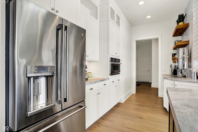 kitchen with appliances with stainless steel finishes, light wood-style flooring, light stone counters, and open shelves