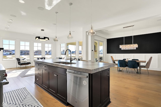 kitchen featuring a kitchen island with sink, light wood-style flooring, a sink, dishwasher, and pendant lighting