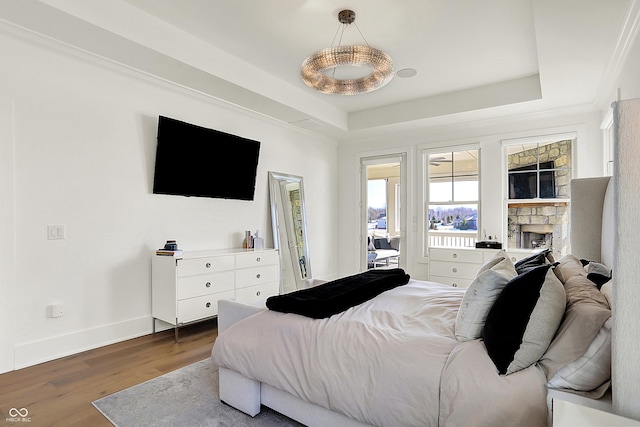 bedroom featuring a stone fireplace, wood finished floors, a raised ceiling, and baseboards