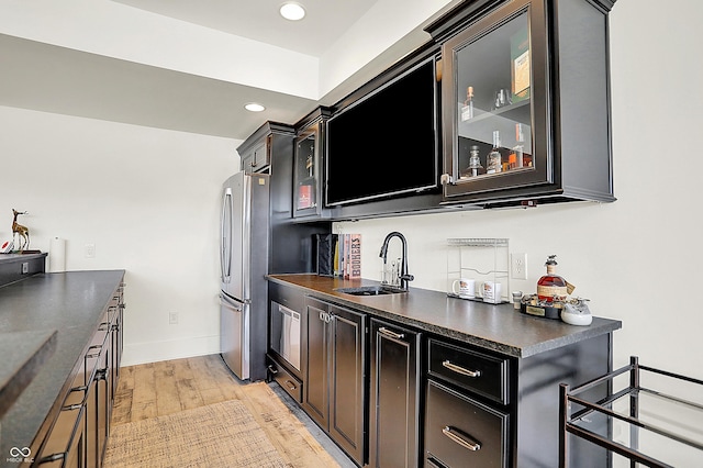 kitchen with light wood-style flooring, a sink, freestanding refrigerator, dark countertops, and glass insert cabinets