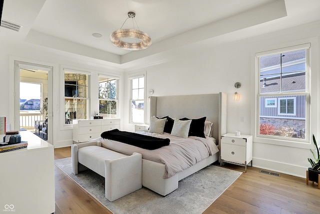 bedroom with a tray ceiling, wood-type flooring, and visible vents