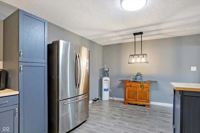 kitchen with a textured ceiling, baseboards, freestanding refrigerator, wood tiled floor, and pendant lighting