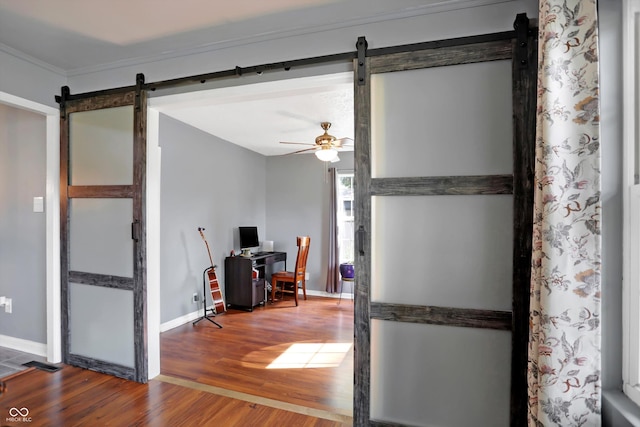 interior space featuring crown molding, a barn door, ceiling fan, wood finished floors, and baseboards