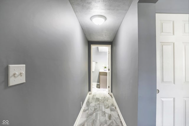 hallway featuring marble finish floor, a textured ceiling, and baseboards