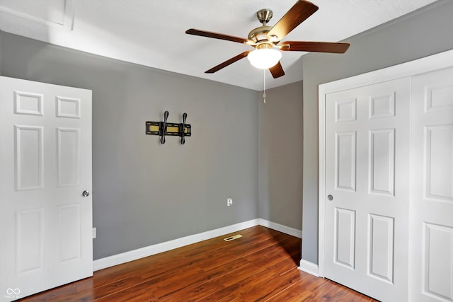 unfurnished bedroom featuring visible vents, baseboards, a ceiling fan, dark wood-style floors, and a closet