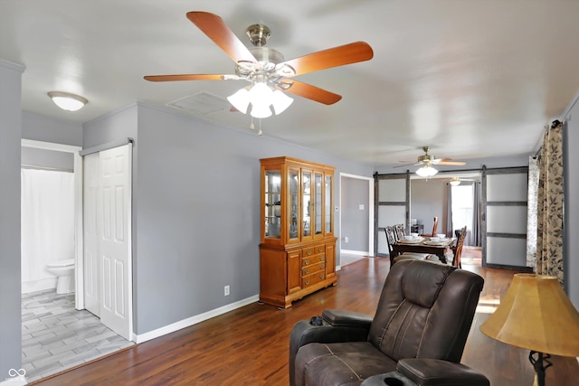 living area with a barn door, wood finished floors, a ceiling fan, and baseboards