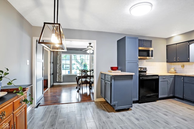 kitchen featuring wood finish floors, light countertops, stainless steel microwave, decorative backsplash, and black / electric stove