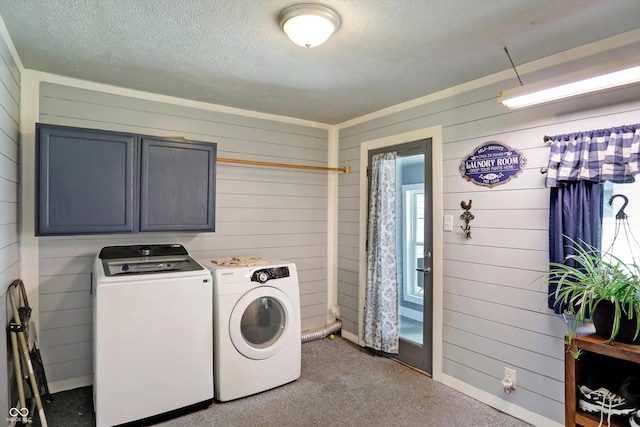 laundry room with a textured ceiling, washer and clothes dryer, cabinet space, and wooden walls