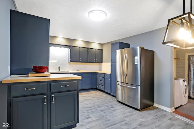 kitchen featuring tasteful backsplash, wood counters, freestanding refrigerator, blue cabinets, and a sink