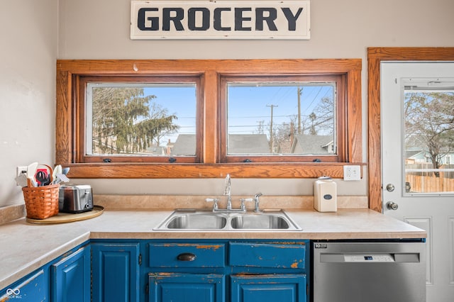 kitchen featuring light countertops, stainless steel dishwasher, a sink, and blue cabinets