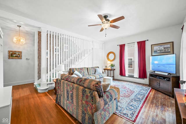 living area with stairs, baseboards, wood finished floors, and ceiling fan with notable chandelier