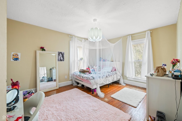 bedroom featuring a notable chandelier, a textured ceiling, baseboards, and wood finished floors