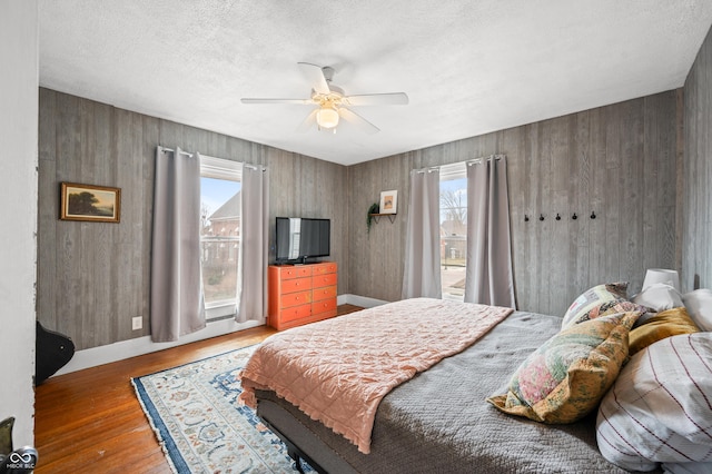 bedroom with ceiling fan, wooden walls, a textured ceiling, wood finished floors, and baseboards