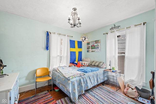 bedroom featuring a notable chandelier, a textured ceiling, baseboards, and wood finished floors