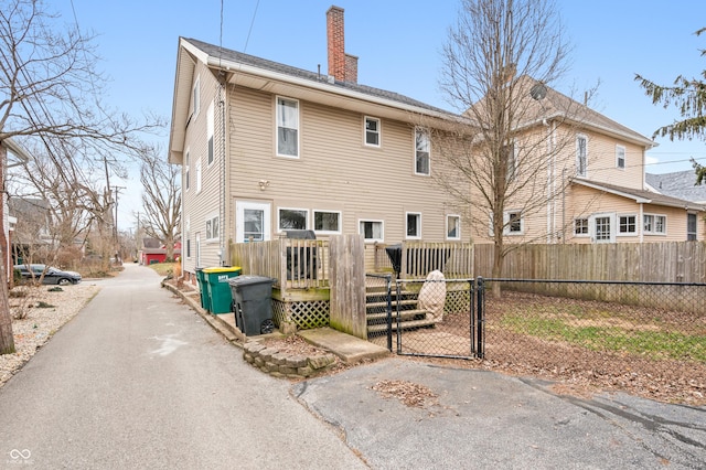 back of property featuring a wooden deck, a chimney, fence, and a gate