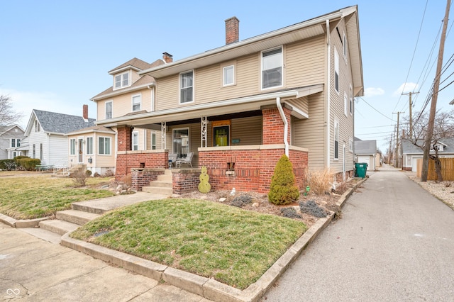 view of front facade with covered porch, brick siding, an outdoor structure, a front lawn, and a chimney