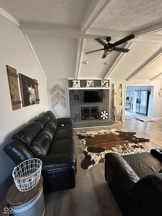 living area featuring vaulted ceiling with beams, a fireplace, wood finished floors, and a ceiling fan