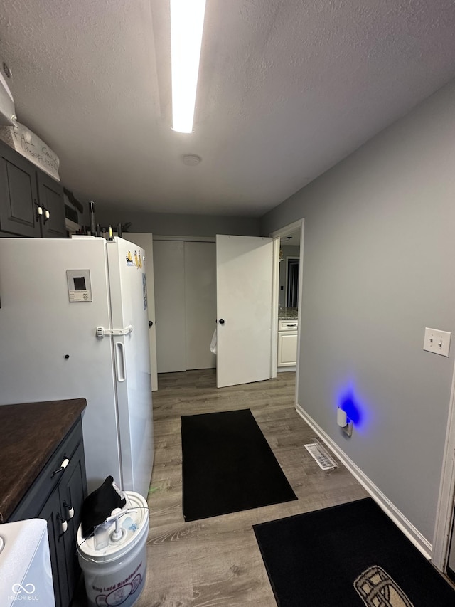 kitchen featuring visible vents, dark countertops, freestanding refrigerator, a textured ceiling, and light wood-style floors