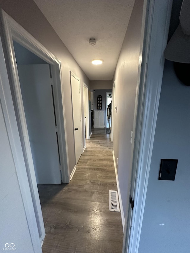 hallway with dark wood-style floors, baseboards, visible vents, and a textured ceiling