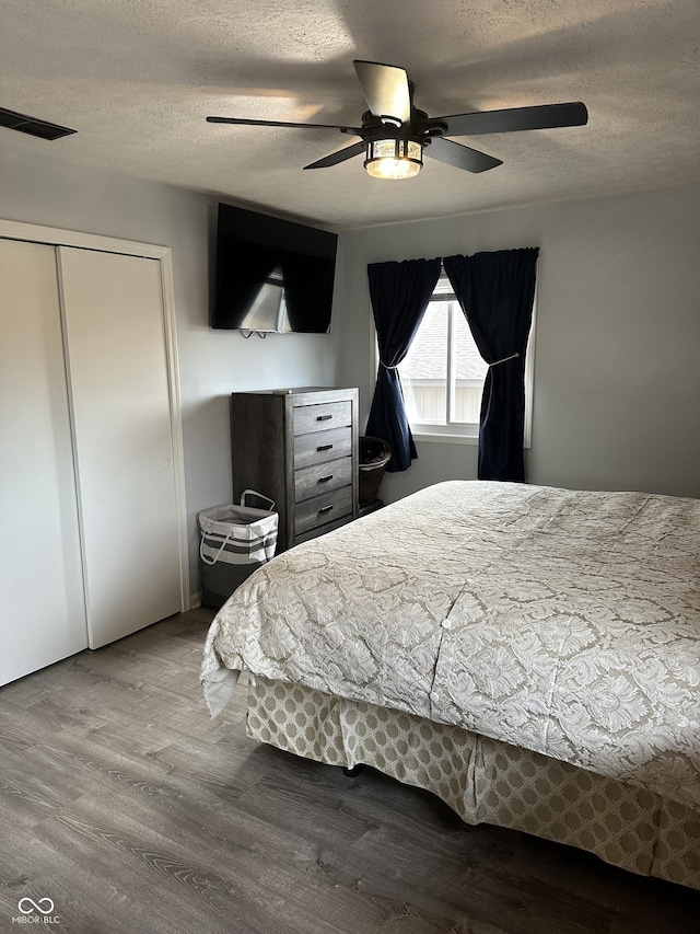 bedroom featuring a closet, visible vents, a ceiling fan, a textured ceiling, and wood finished floors