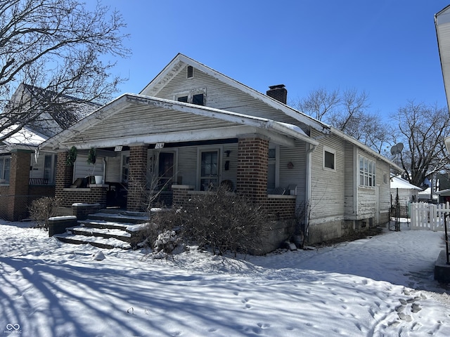 view of front of house featuring a porch, brick siding, fence, and a chimney