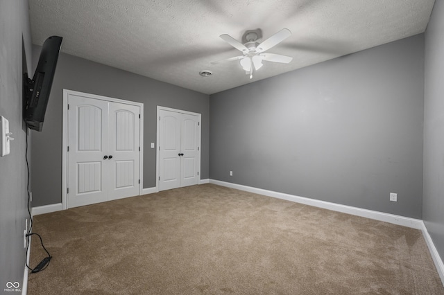 unfurnished bedroom featuring carpet floors, a textured ceiling, baseboards, and multiple closets